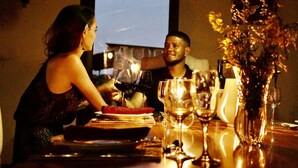 A dining table with wine glasses, a vase with flowers, and a television screen in the background.