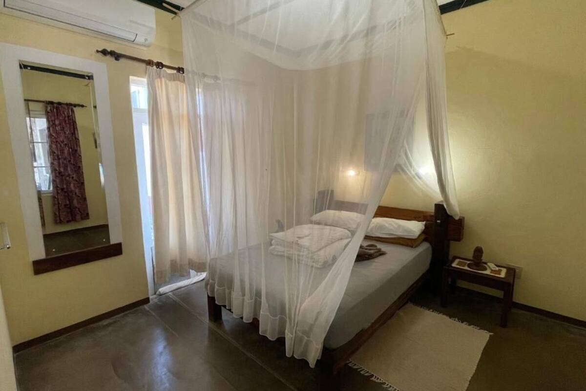 A bedroom with a bed under a mosquito net, a bedside table, and a nightstand.
