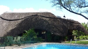 A swimming pool with a thatched roof structure and a lounge area with green chairs.