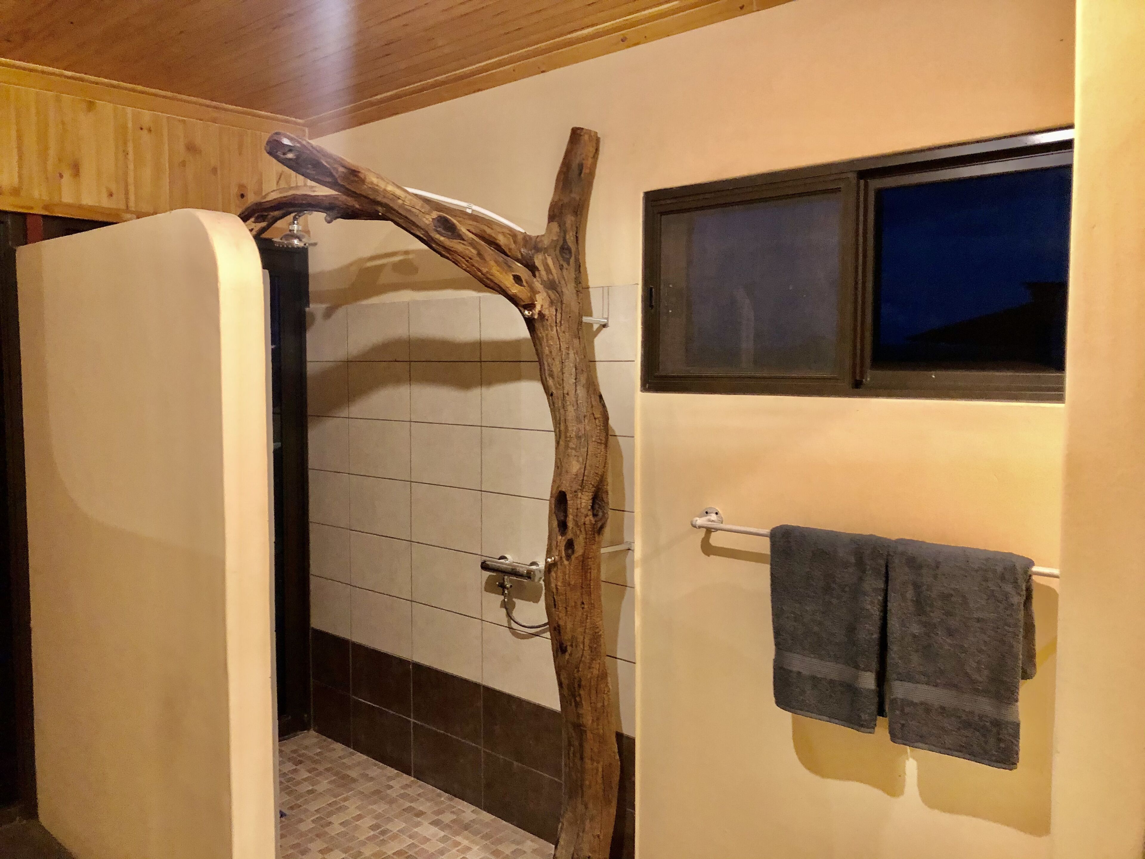 A bathroom with a wooden branch wall decoration, a towel rack with two towels, and a window above the sink.