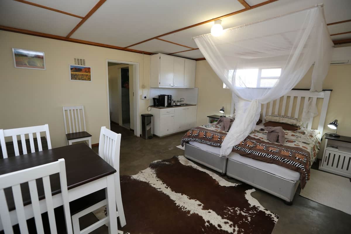 A bedroom with a canopy bed, a dining table with chairs, a kitchen area, and a bathroom.