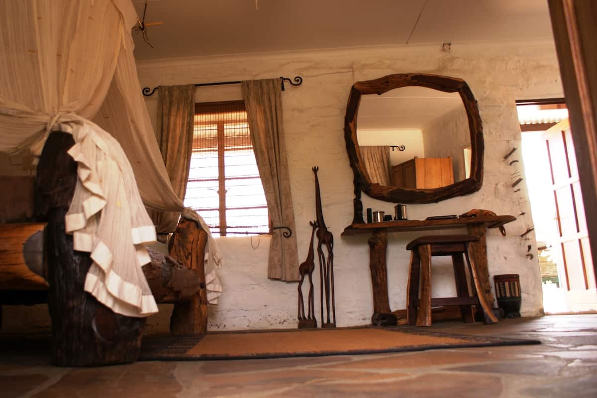 A rustic bedroom with a wooden bed, a canopy, a mirror, and a window with curtains.
