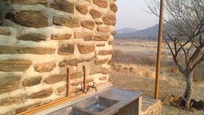 A stone wall with a metal sink and faucet, a wooden post, and a view of a dry landscape with mountains in the distance.