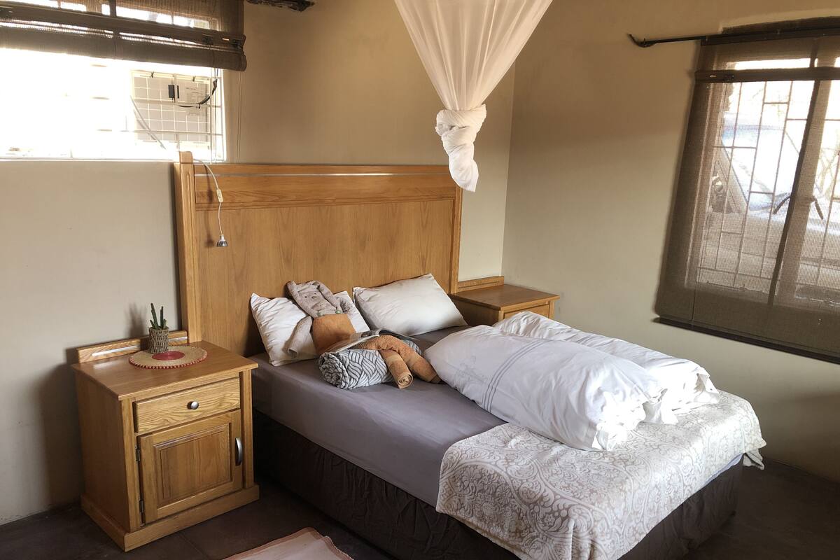 A bedroom with a wooden headboard, a canopy bed, a nightstand, and a bedside table.