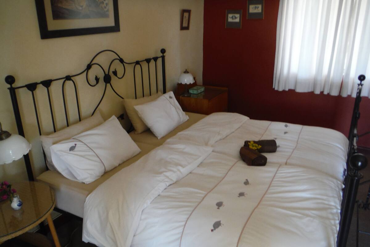 A neatly made bed with white linens and decorative pillows, a bedside table with a lamp, and a framed picture on the wall.