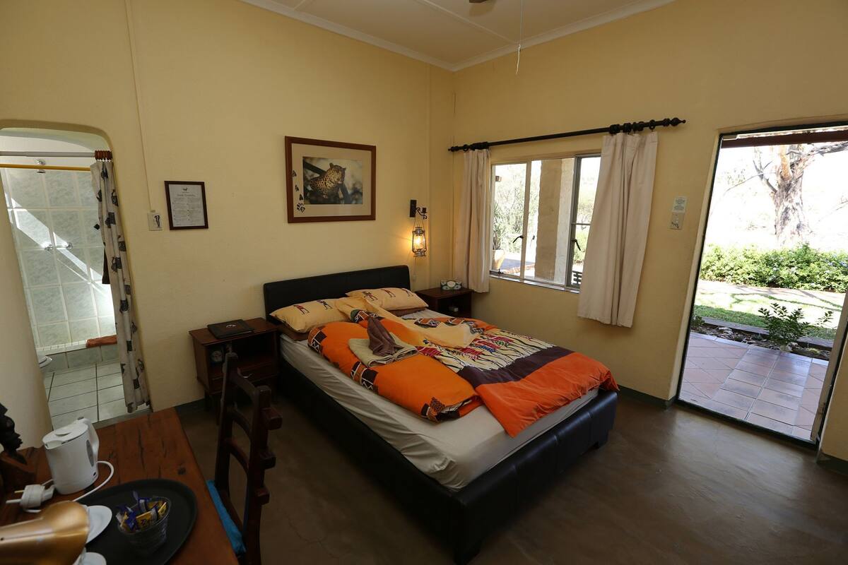 A bedroom with a bed, bedside table, lamp, and a view of the outside.