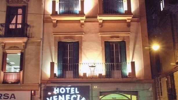 Un hotel con fachada clásica, varios balcones y una entrada bien iluminada.