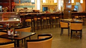 Un restaurante con varias mesas y sillas, una zona de bar y un amplio ventanal con vistas a la ciudad.