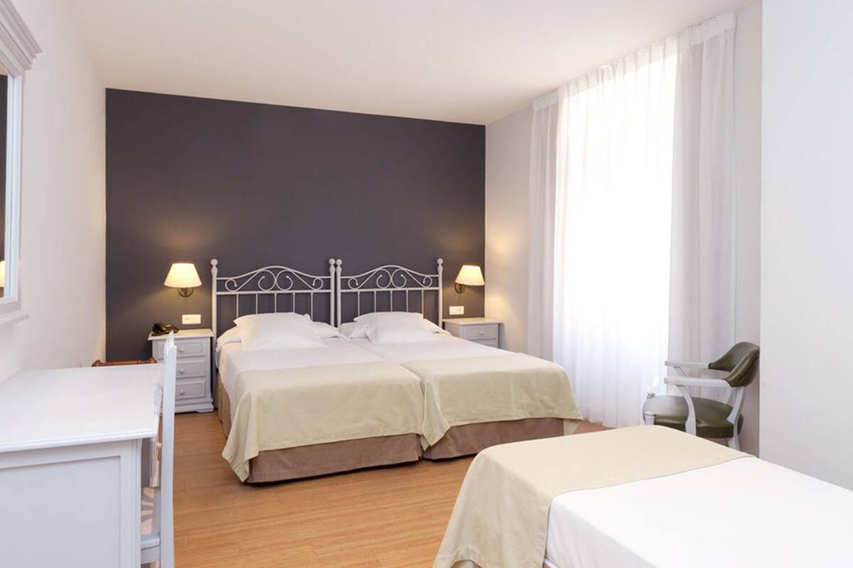 A hotel room with two beds, a desk, and a chair.