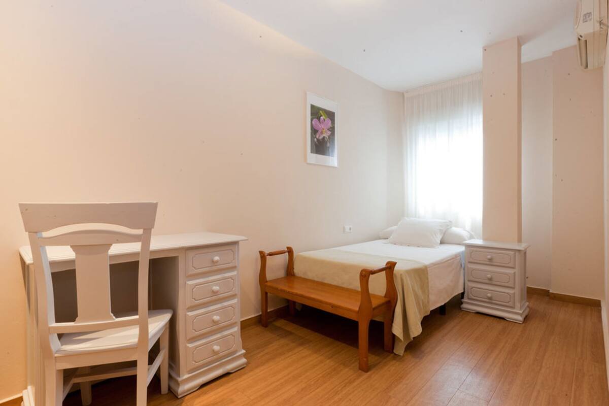 A bedroom with a bed, a wooden bench, a dresser, and a nightstand.