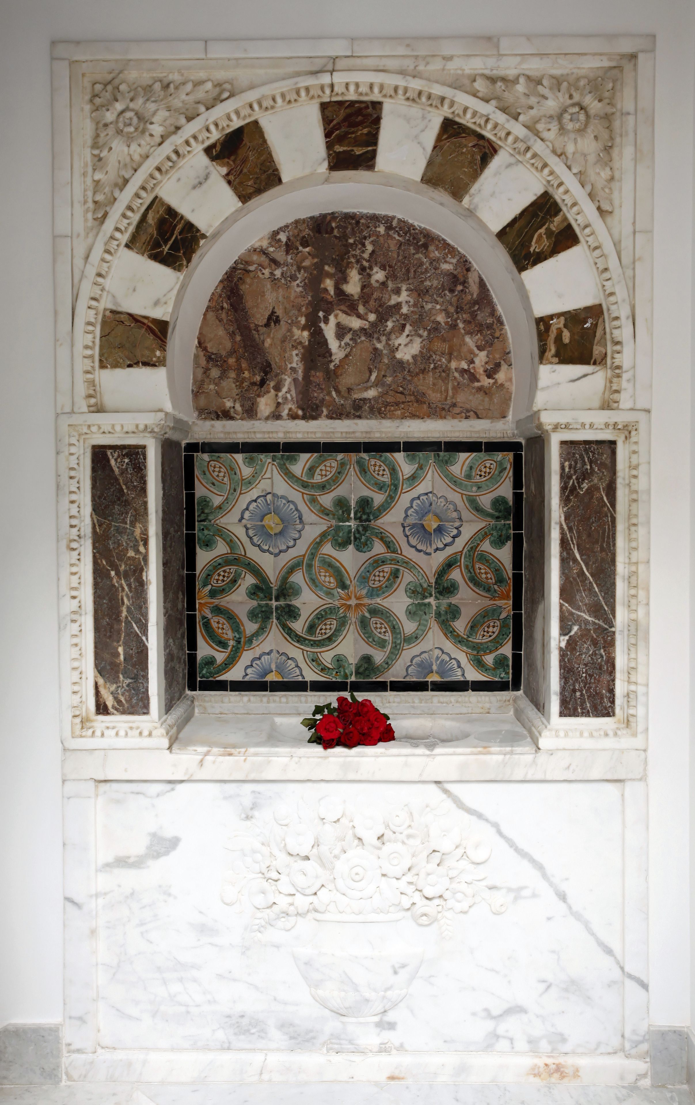 A marble fireplace with intricate floral tile design and a red rose on the mantel.