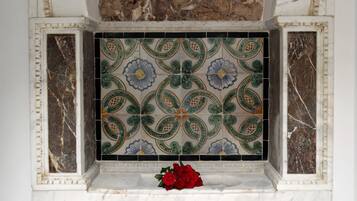 A marble fireplace with intricate floral tile design and a red rose on the mantel.