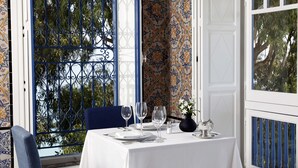 A dining table set with white tablecloth, plates, and wine glasses, with a blue chair and a vase of flowers. - La Villa Bleue (Sidi Bou Said)