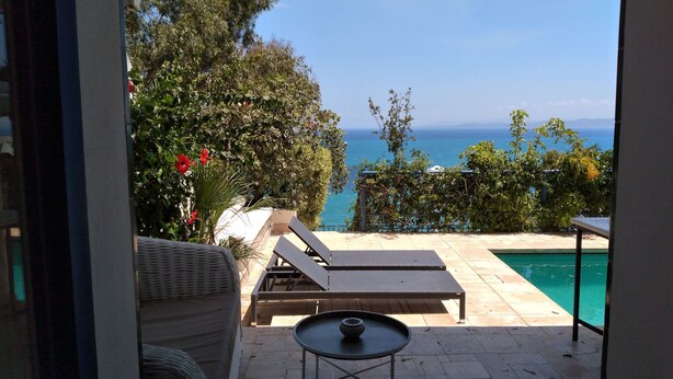 A patio with a pool, lounge chairs, and a view of the sea. - La Villa Bleue (Sidi Bou Said)
