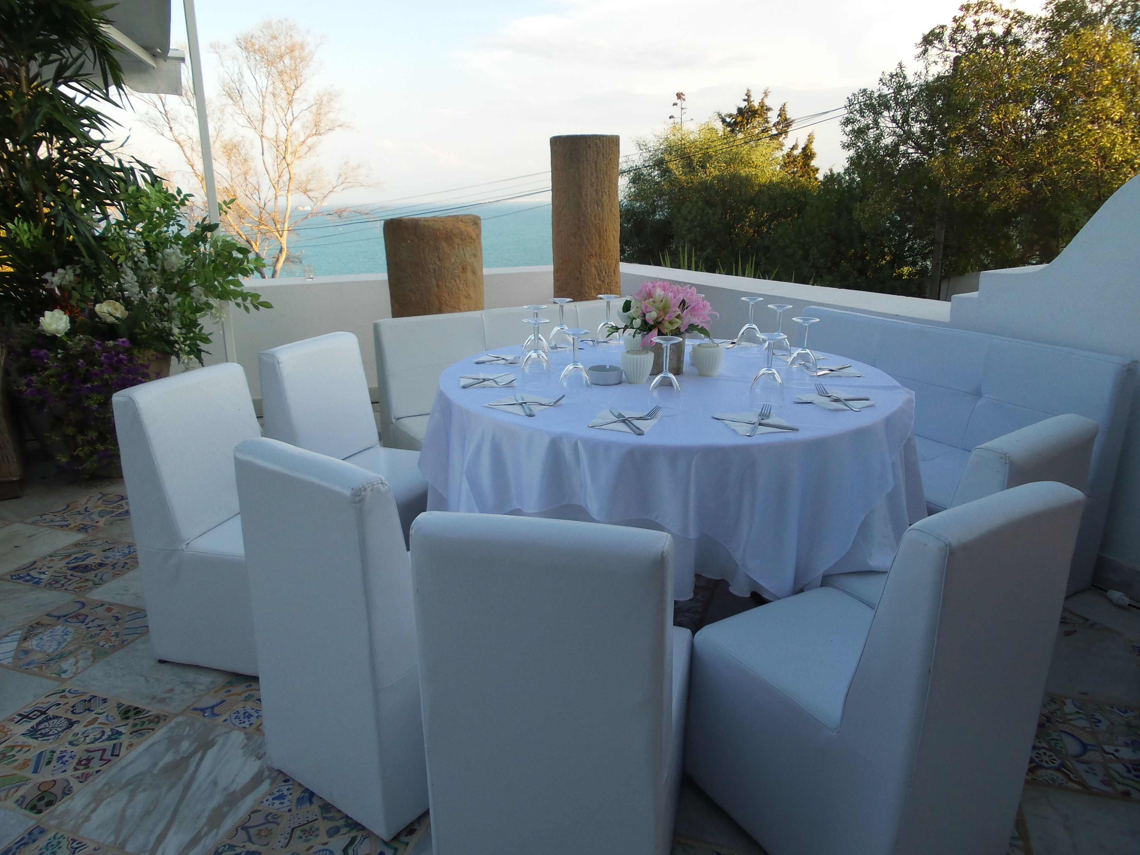 Una mesa redonda dispuesta para seis personas, con sillas blancas, mantel blanco y un centro de mesa floral.