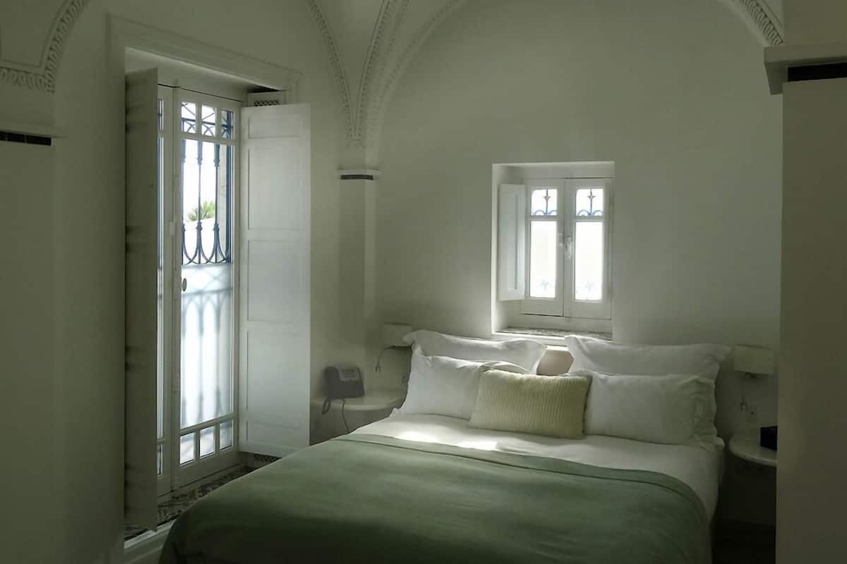 A bedroom with a large bed, a window, and a door with a view of the outside.