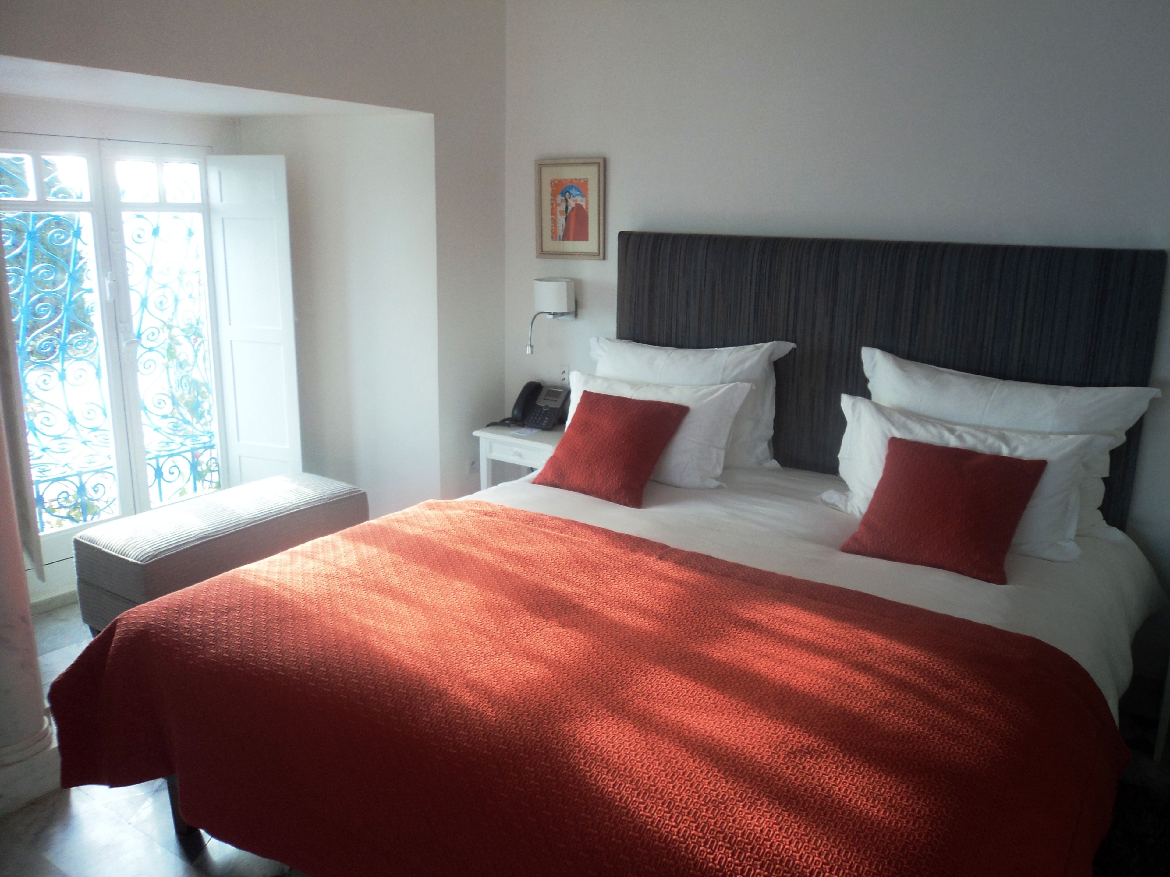 Habitación de hotel con una cama grande, dos almohadas, una mesita de noche con teléfono y una ventana con vistas.