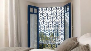 A bedroom with a bed, a window with a blue frame, and a decorative metal screen. - La Villa Bleue (Sidi Bou Said)