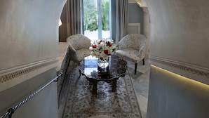 A staircase leading to a room with two patterned armchairs, a glass coffee table with a vase of flowers, and a view through a large window. - La Villa Bleue (Sidi Bou Said)