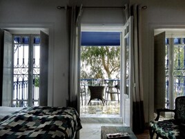 Habitación de hotel con una cama, una mesita y una silla. Tiene un balcón con una mesa y sillas afuera.