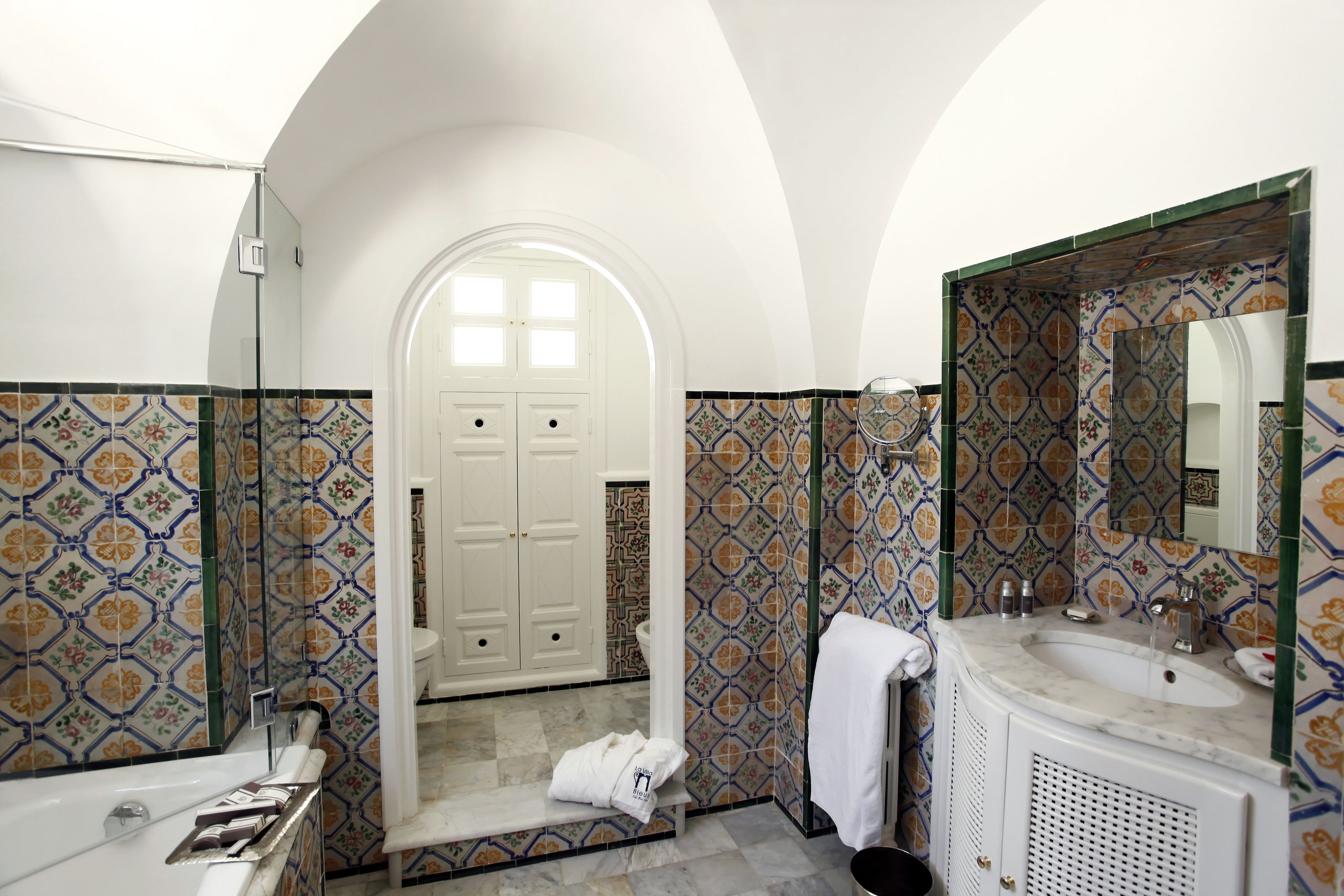 Une salle de bain avec une baignoire, un lavabo et un miroir. Une porte donne accès à une autre pièce.