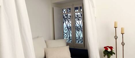 A bedroom with a bed under a canopy, a nightstand with candles, and a window with decorative ironwork.