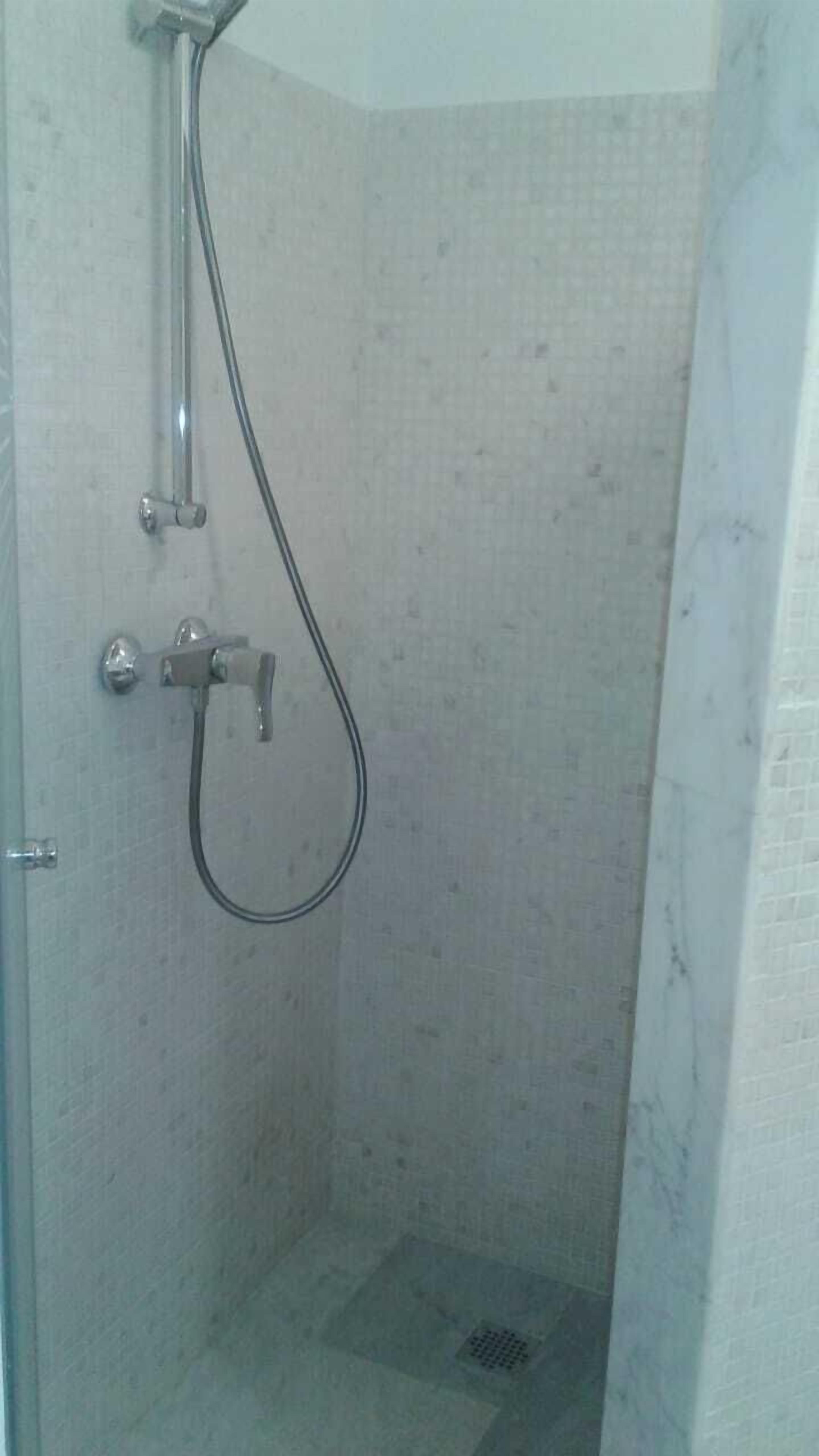 A small, enclosed shower area with a showerhead and a handheld shower attachment.