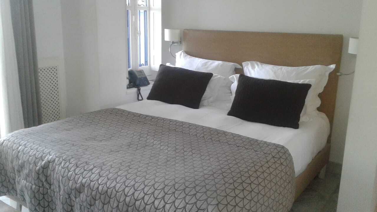 Un lit bien fait, avec une couvre-lit à motifs, une tête de lit en bois et deux oreillers noirs.