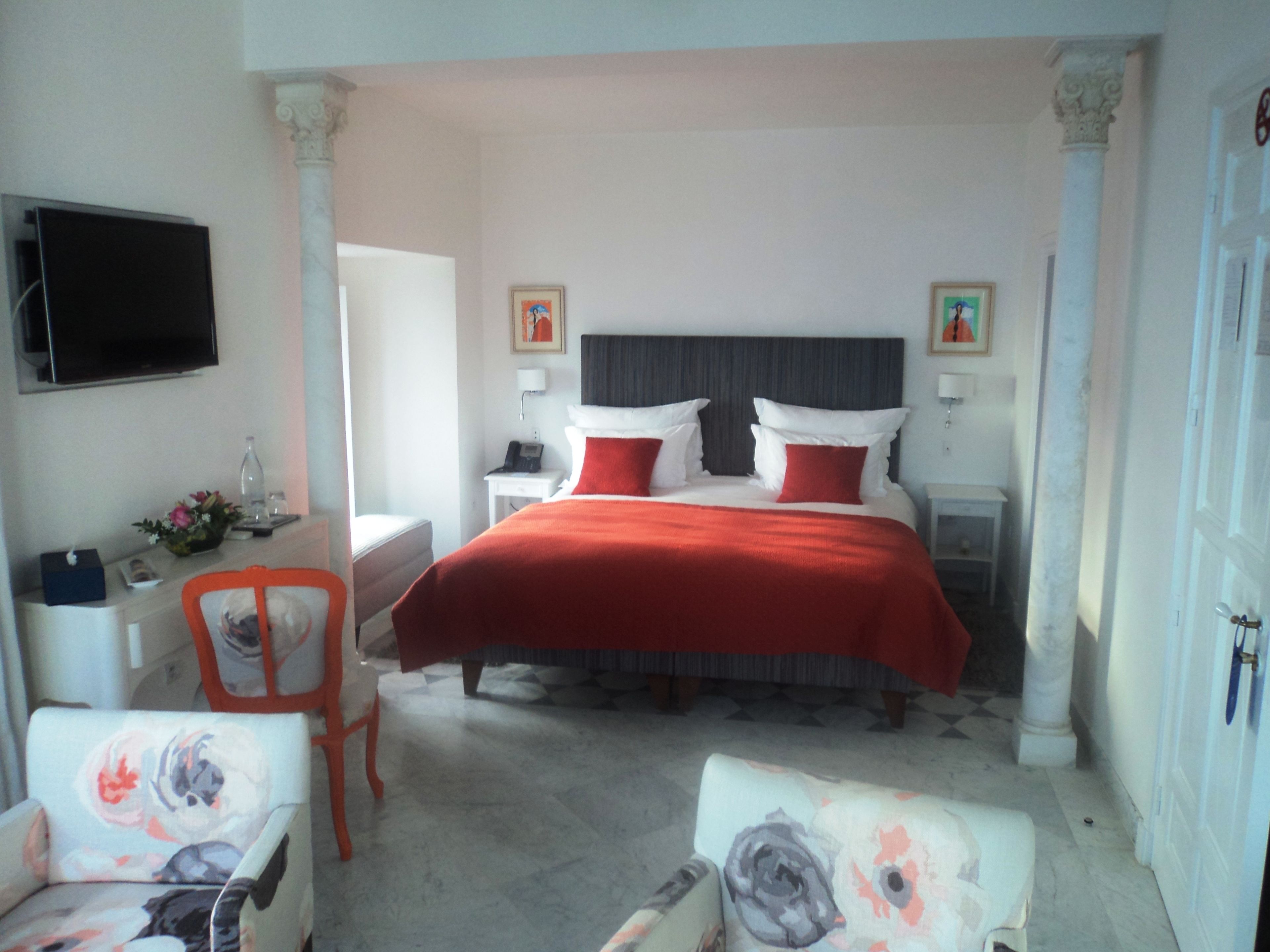 A hotel room with a bed, two bedside tables, a chair, a desk, a television, and a door.