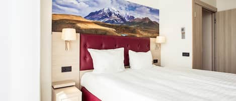 A hotel room with a large bed, a red headboard, and a mountain landscape painting on the wall.