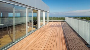 Un edificio moderno con amplios ventanales de vidrio, una terraza de madera y vistas al océano.