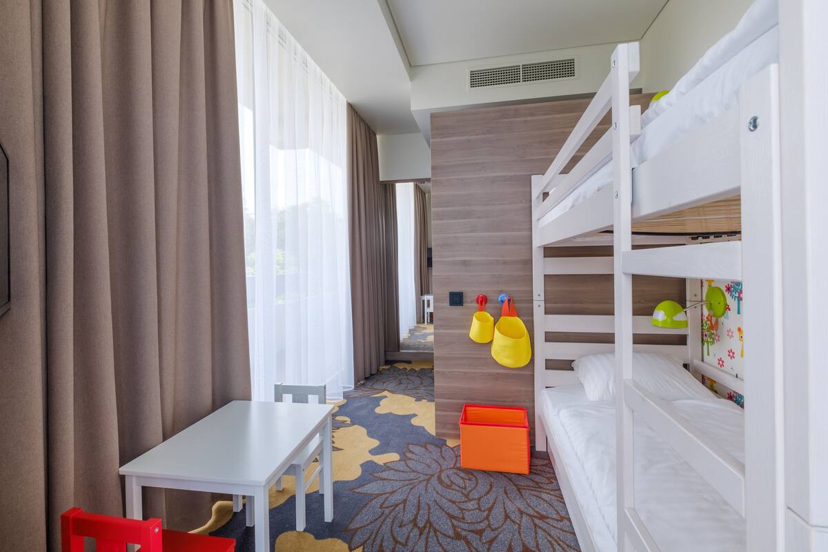 Ein Hotelzimmer mit Etagenbetten, einem kleinen Tisch, einem roten Stuhl und einem farbenfrohen Teppich.