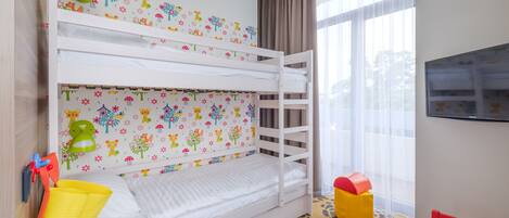 A bunk bed room with a patterned wall, a television, and a table with a chair.