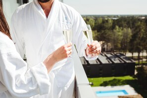 Una persona con bata sostiene dos copas de champán, con vistas a una piscina y follaje.