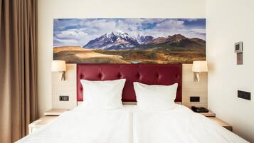 A hotel room with a large bed, two bedside lamps, a mounted TV, and a painting of a mountain landscape.
