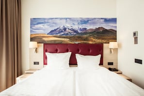 Relax in comfort with a large bed and two bedside lamps, accompanied by a serene mountain view.