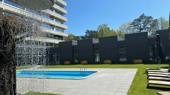 Un edificio moderno con piscina, rodeado de un césped cuidado y una fuente.