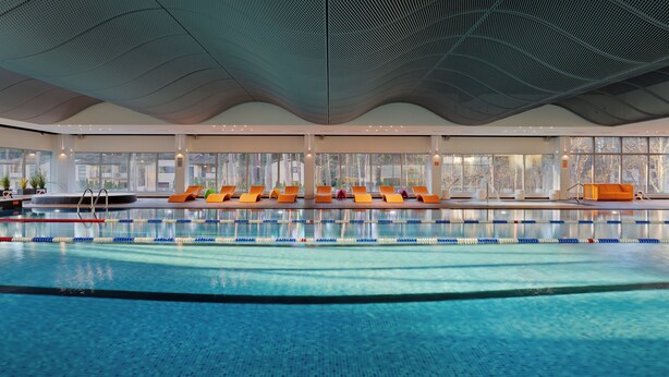 Una piscina interior con carriles delimitados, un área de descanso con sillas color naranja y ventanas amplias que ofrecen vistas al exterior.