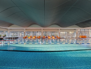An indoor swimming pool with clear lanes, a lounge area with orange chairs, and large windows offering views of the outside. - SemaraH Hotel Lielupe SPA & Conferences (Jurmala)