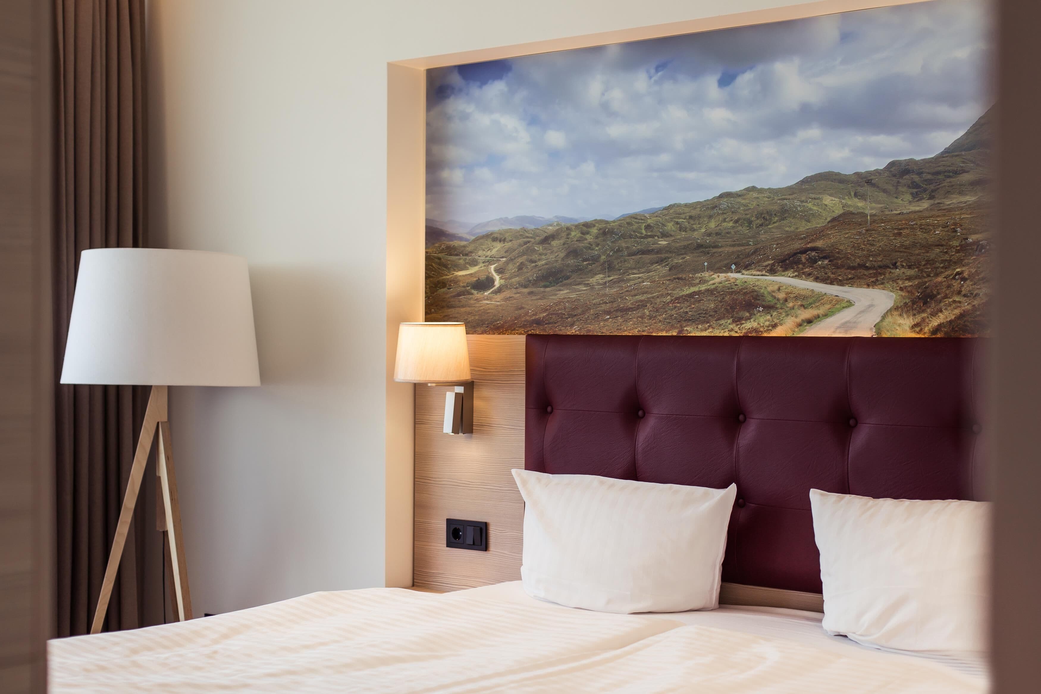 Habitación de hotel con una cama grande, cabecero, lámpara y luz empotrada en la pared.
