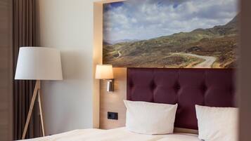 Habitación de hotel con una cama grande, cabecero, lámpara y luz empotrada en la pared.