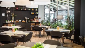 Un restaurante moderno con varias mesas y sillas, grandes lámparas colgantes y una variedad de plantas y decoraciones.
