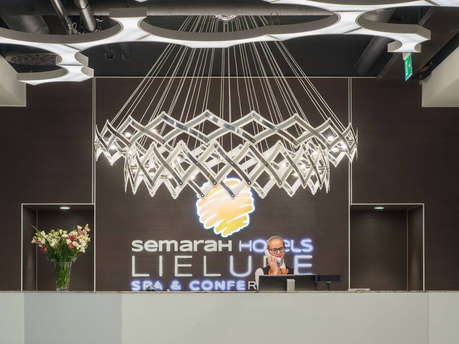 A reception desk with a modern chandelier, a logo for Semarah Hotels, and a vase of flowers.