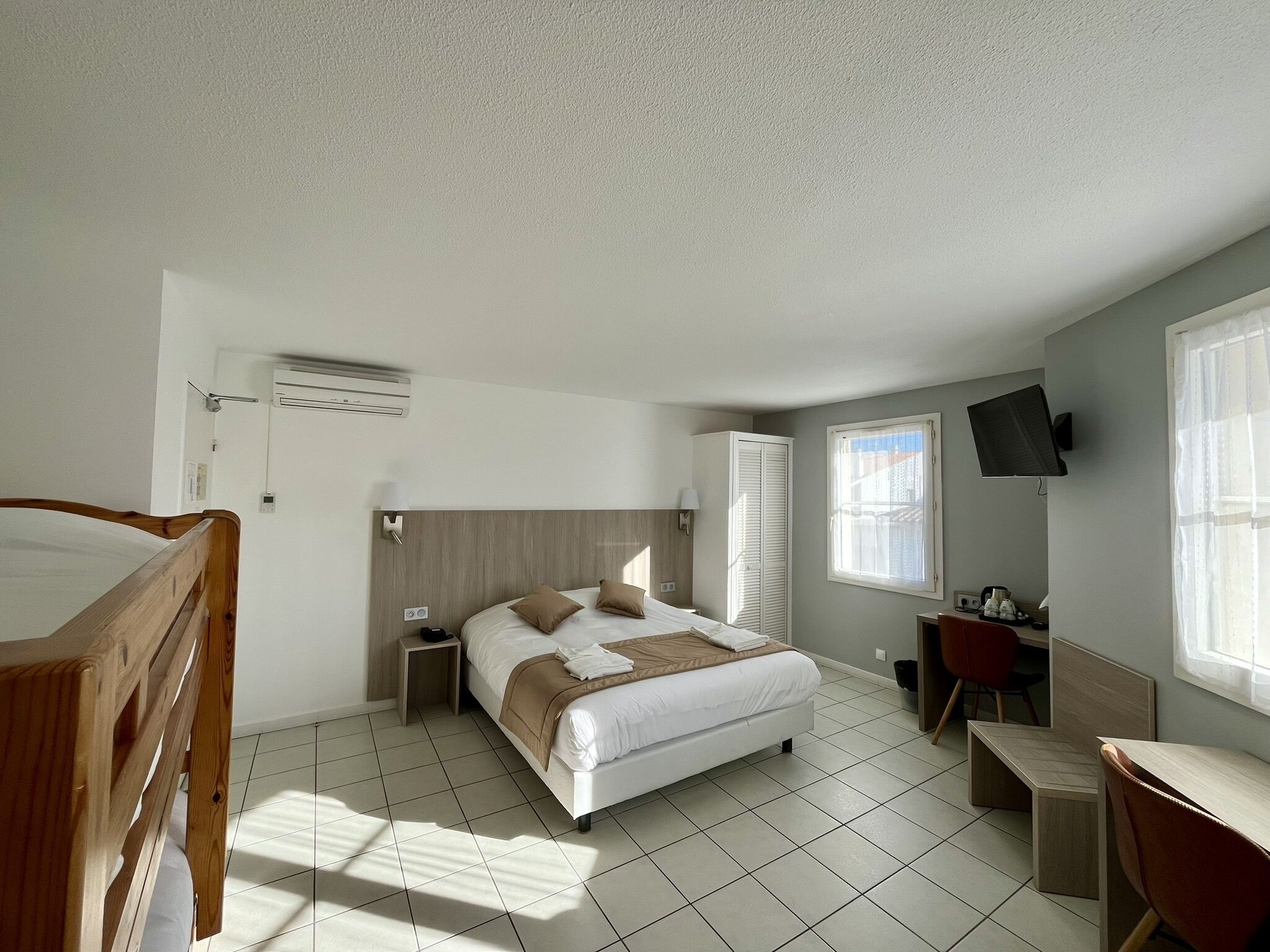 Una camera d'albergo con un letto, comodini, una scrivania, una sedia, televisione e finestre.