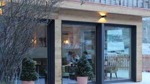 A modern building with large glass doors, a wooden facade, and two potted Christmas trees in front. - Hotel Welschen Zermatt (Zermatt)