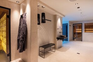 A modern bathroom with a bench, towel rack, and a glass shower area. - Hotel Welschen Zermatt (Zermatt)