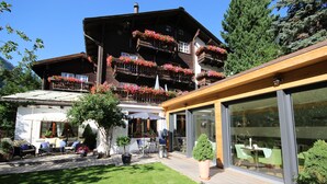 A modern building with a wooden deck, outdoor seating, and flower boxes on balconies. - Hotel Welschen Zermatt (Zermatt)