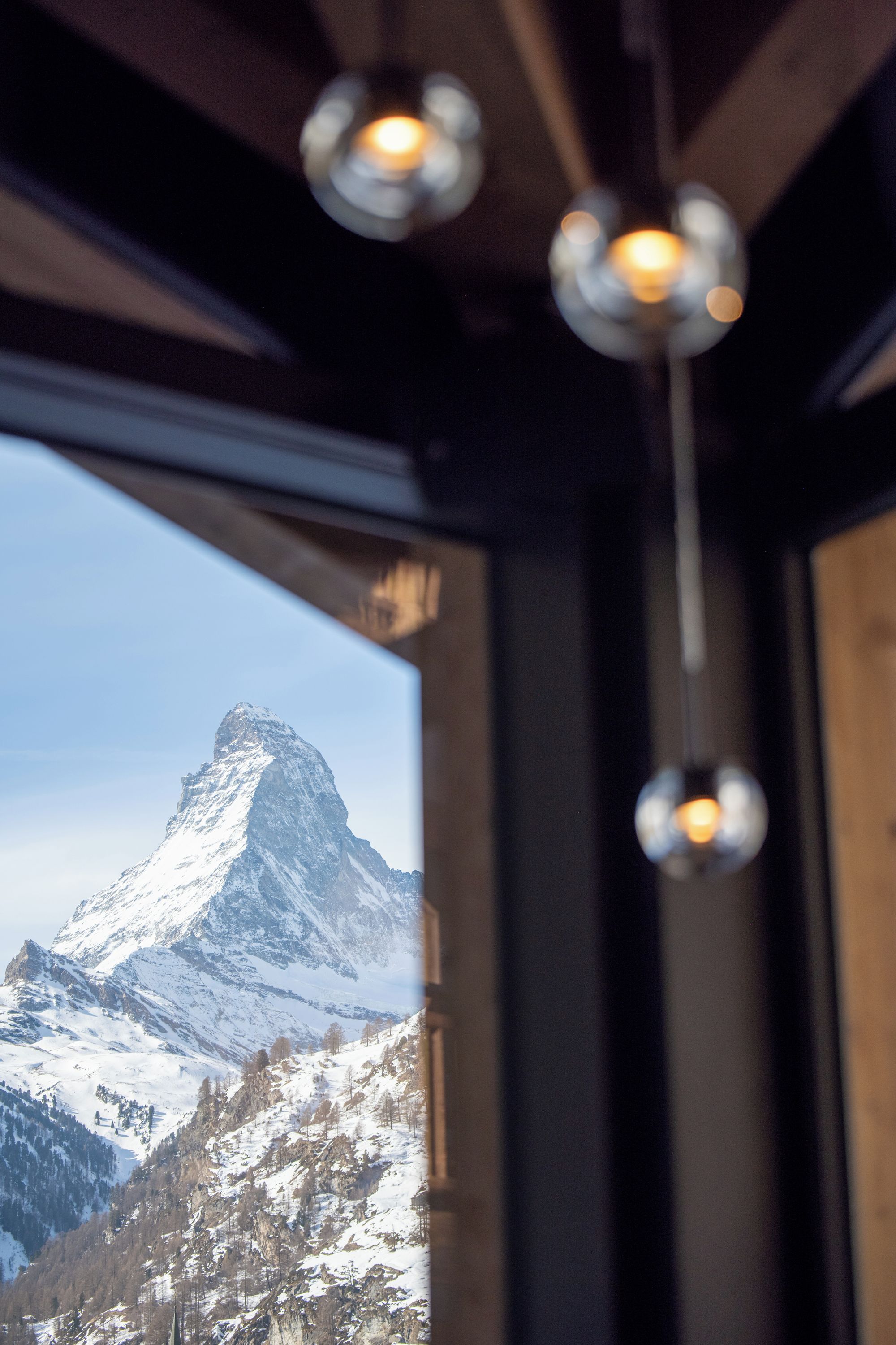 Blick auf Berge durch ein Fenster mit hängenden Lampen.