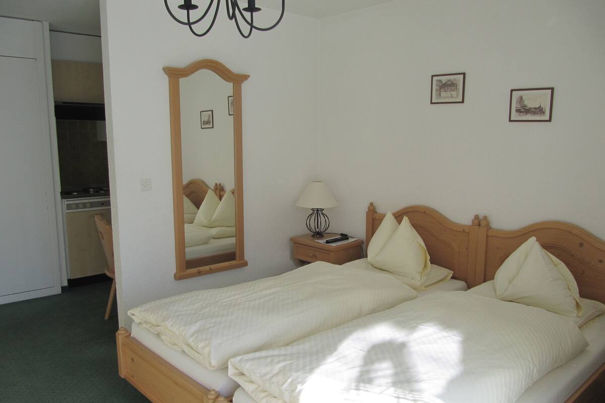 A bedroom with a wooden bed, a nightstand with a lamp, a mirror, and a small desk with a chair.