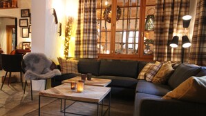 A cozy living room with a sofa, a coffee table, and a chair. There are plaid curtains and a window with a view of trees. - Hotel Welschen Zermatt (Zermatt)